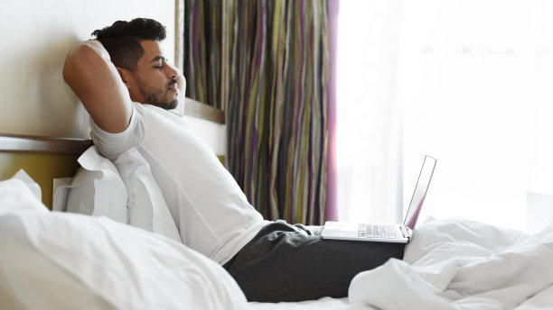 在床上听音乐、使用笔记本电脑的放松帅哥图片下载