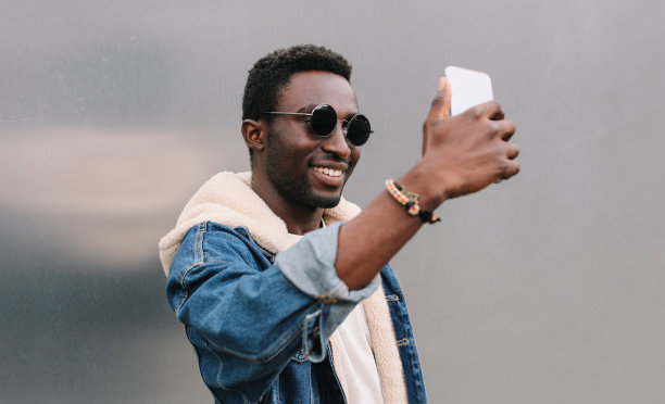 快乐微笑的非洲男子用智能手机在灰色墙壁上自拍的特写照片图片下载