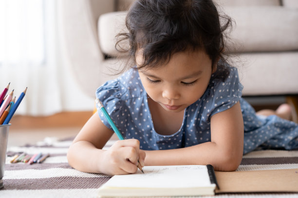 一个亚洲小女孩躺在她家客厅的地毯上画画图片下载