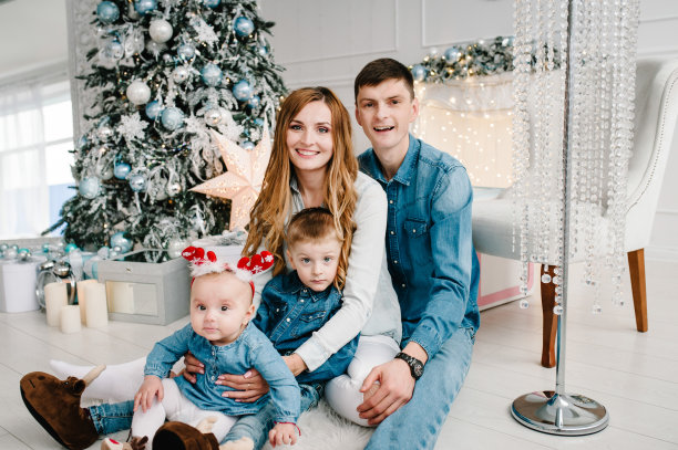 爸爸、妈妈抱着儿子和女儿靠近圣诞树。新年快乐，圣诞快乐。圣诞装饰室内。家庭度假的概念。关闭了。图片下载