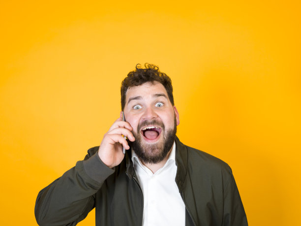 黑胡子黑头发的酷男人拿着智能手机在橙色背景前摆造型图片下载