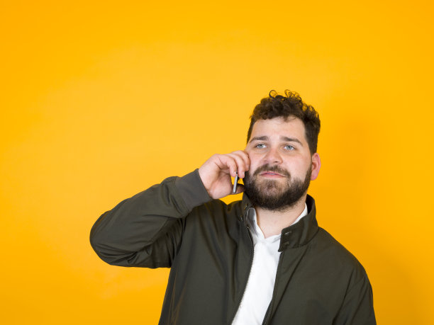 黑胡子黑头发的酷男人拿着智能手机在橙色背景前摆造型图片下载