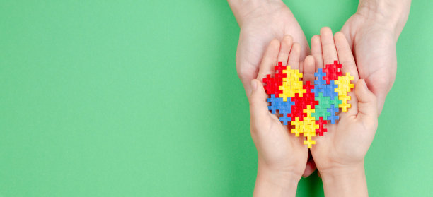 在绿色的背景下，大人和小孩手牵着彩色的心。世界自闭症宣传日的概念图片下载