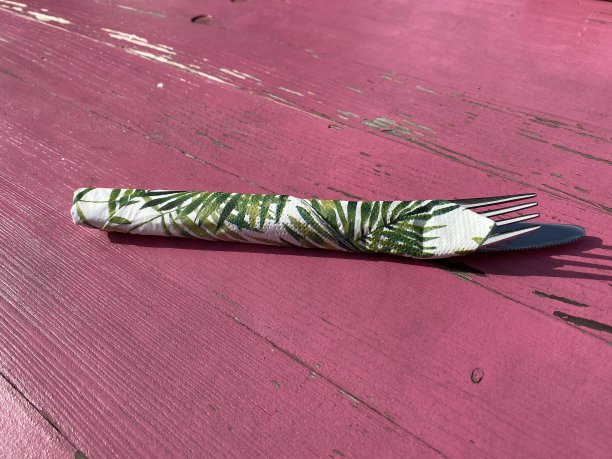 用棕榈叶餐巾包着的刀叉放在粉红色的桌子上图片下载