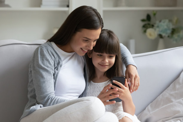 快乐女人抱着可爱的小女儿，一起玩手机。图片下载
