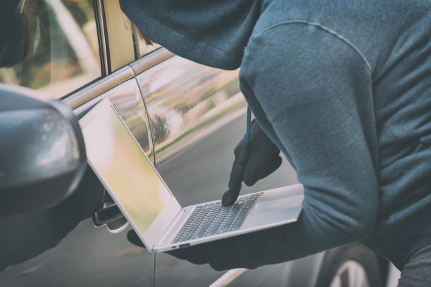 蒙面小偷试图用笔记本电脑破坏汽车的安全系统。图片下载