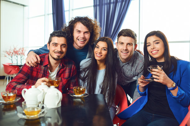 朋友们坐在咖啡馆的一张桌子旁看着镜头。图片下载