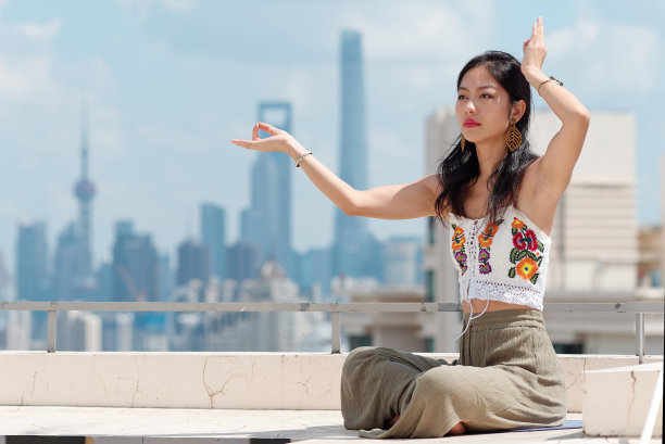 身穿运动服的漂亮中国女人在楼顶练习瑜伽和冥想，以上海天际线为背景，年轻女性在阳光明媚的城市里做瑜伽体式。素材图片