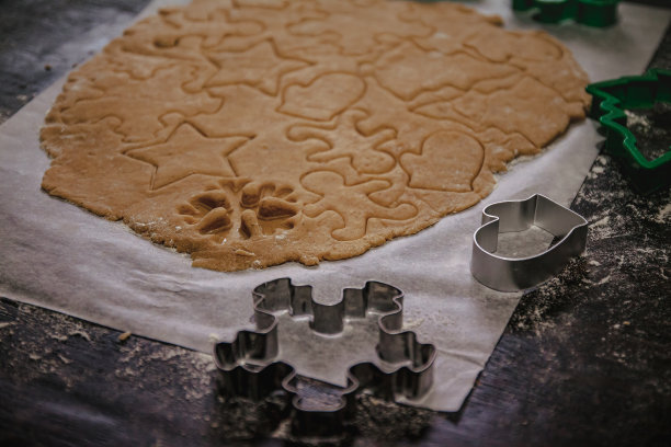在烤盘纸上，以黑色为背景，从生面团中切出一棵圣诞树、星星、小矮人、心形的姜饼。前视图。节省空间图片下载
