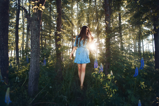 一个神话般的年轻女子在落日的余晖中走在森林里。图片下载