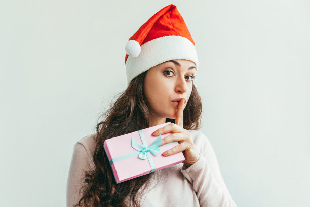 美丽的女孩在红色的圣诞老人帽拿着礼物盒孤立在白色的背景图片下载