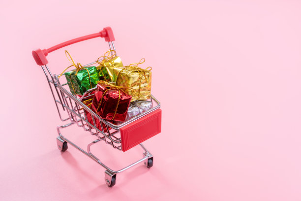年度销售，圣诞购物季概念-迷你红色购物车装满礼物盒孤立在淡粉色背景，拷贝空间，关闭图片下载
