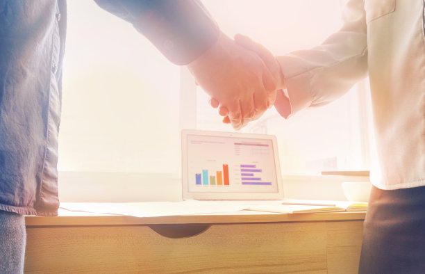 业务握手与背景图表数据在笔记本电脑屏幕和阳光从窗口图片下载