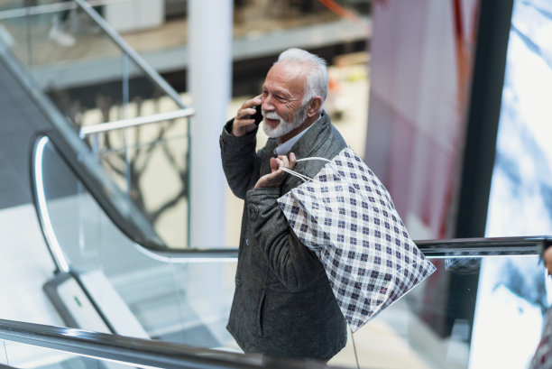 购物时间。拿着购物袋的现代老人正在打电话。消费主义、购物、生活理念。老人购物。全神贯注的英俊的中年商人手里拿着一个手机图片下载