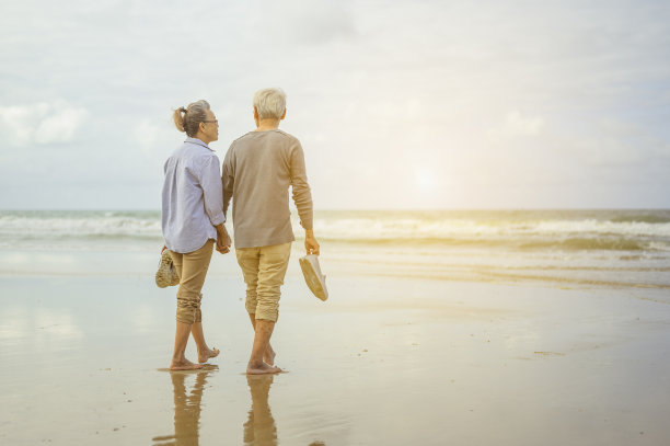 老年夫妇在日出时手拉手在海滩上散步，计划退休时的人寿保险概念。图片下载