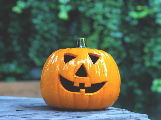 万圣节南瓜在木桌上用绿色的叶子作背景和暗光。图片下载