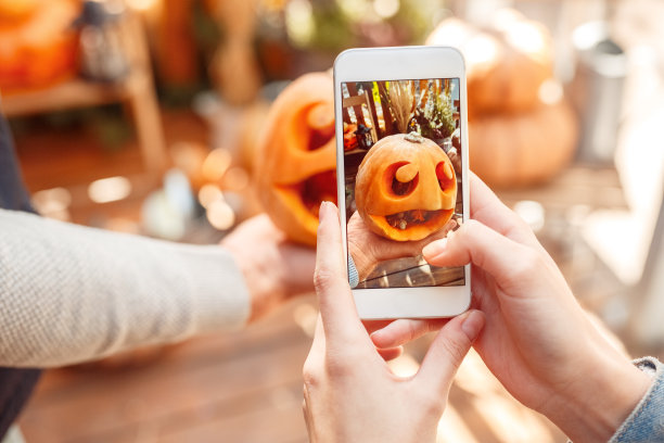 年轻的成年人朋友在智能手机上制作照片雕刻的南瓜图片下载