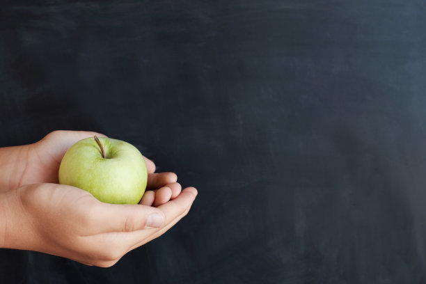 学生手捧绿苹果，以黑板为背景，祝教师节快乐图片下载
