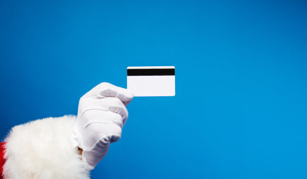 圣诞购物。一张信用卡的特写照片，被圣诞老人拿在右手里戴着白手套，圣诞老人正站在左边。图片下载