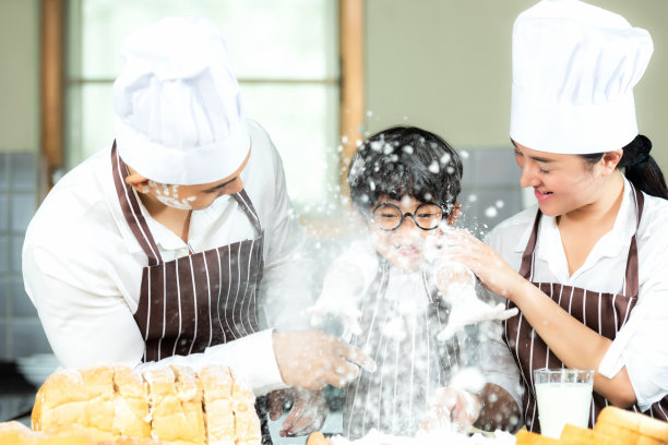 家庭生活方式。厨师亚洲妈妈靠在父亲身上，帮助他们的儿子烹饪烤面包和做晚餐的面包。图片下载