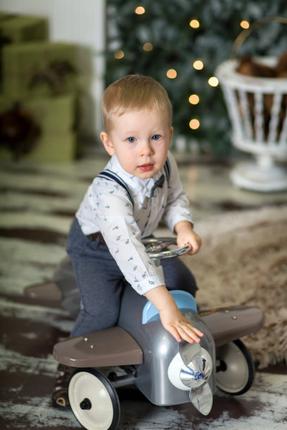 一个小男孩坐在圣诞树旁的老式玩具飞机上的肖像。圣诞装饰品。那男孩对他的圣诞礼物感到高兴。圣诞快乐，2020年新年快乐图片下载
