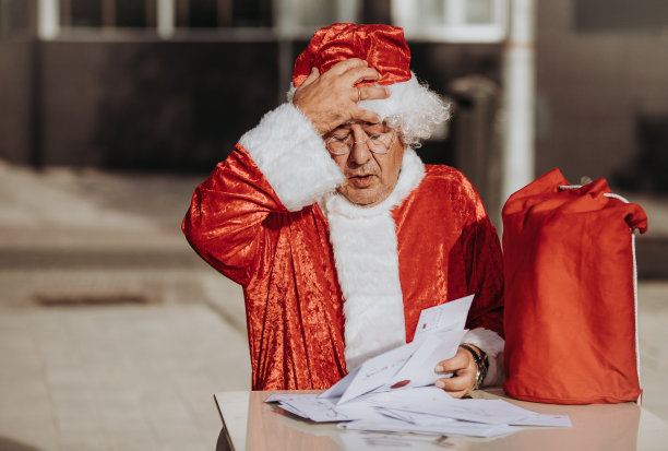 一张没有胡子的圣诞老人坐在露台上整理圣诞卡片的照片，桌子上放着一个红色的袋子。圣诞节的时候图片下载