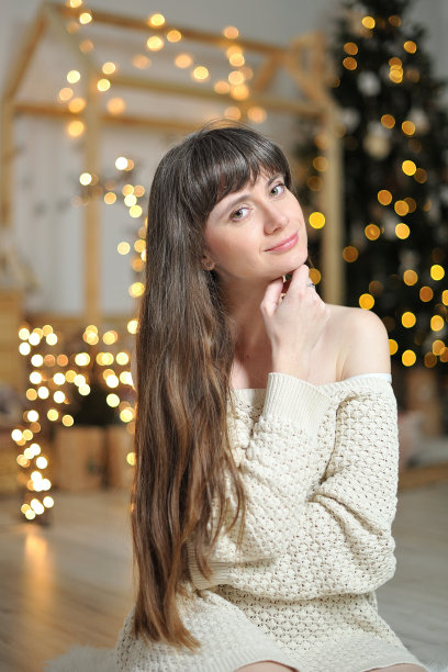 年轻的黑发女孩与长头发在针织毛衣的背景圣诞装饰和散焦图片下载