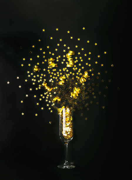 金色星星形状的五彩纸屑和派对彩带从黑色背景的香槟酒杯中倾泻而出。平的风格。庆祝活动的概念。图片下载