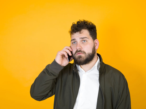 黑胡子黑头发的酷男人拿着智能手机在橙色背景前摆造型图片下载