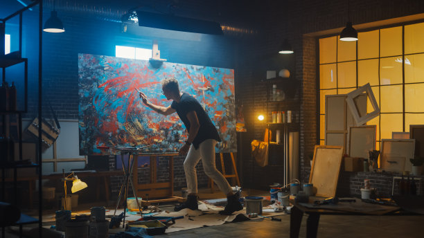 才华横溢的男艺术家，用画笔力作现代油画杰作。黑暗和凌乱的创意工作室与大画布醒目的颜色图片下载