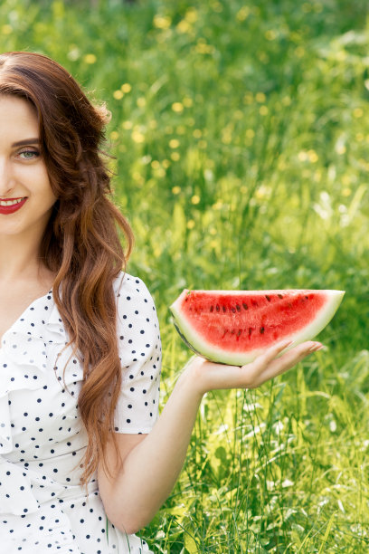 微笑的成年女孩的肖像是在草地上举着西瓜片的背景图片下载