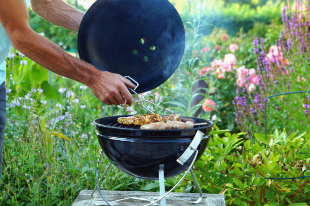 男性的手用一对钳子把美味的烤肉在炭火上烤。一只手在花园里烧烤的细节。图片下载