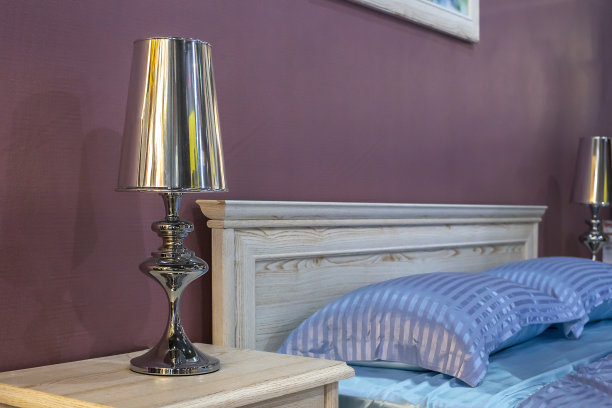 美丽的片段经典豪华卧室内饰与选择性焦点。床上有蓝色的缎子床单和优雅的床头柜，床头柜上有一盏镀铬银的床头灯。图片下载