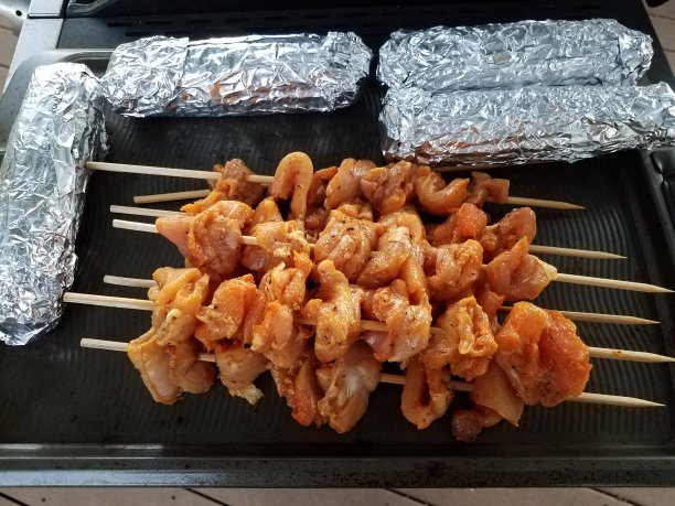 木棒上的生鸡肉和箔纸包裹的玉米放在烤架上图片下载