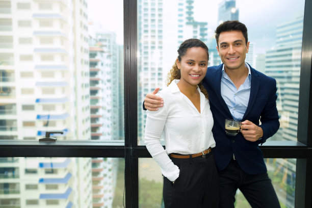 穿着正装的成年商务人士在工作间隙站着放松，在玻璃环绕的现代办公室里喝杯咖啡，还能看到高层建筑。图片下载