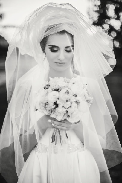 性感创意的肖像美丽的新娘在面纱下抱着花束户外。美丽的新娘穿着白色礼服和现代婚礼花束在夏日公园摆姿势。黑白照片图片下载