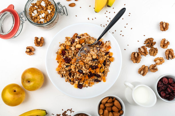 格兰诺拉麦片早餐与牛奶，杏干，蔓越莓，杏仁和亚麻籽在碗上的白色背景。健康的早餐麦片。图片下载