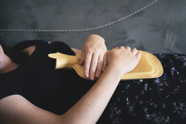 一个生病的女人躺在沙发上，有选择地把热水袋放在肚子上图片下载