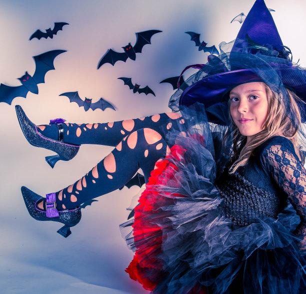 小女孩摆出万圣节女巫服装、女巫帽和女巫鞋的姿势素材图片