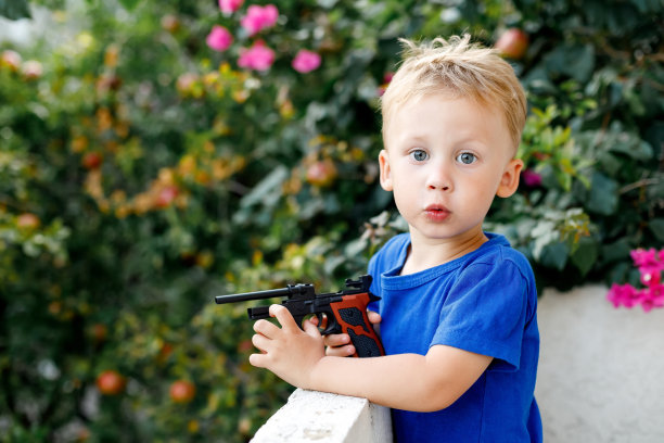 可爱的小男孩和玩具枪在花园里的背景图片下载