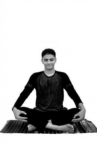 全身镜头的男性青少年在黑色运动服服装孤立在白色和做莲花瑜伽或莲花瑜伽运动交叉双腿。图片下载