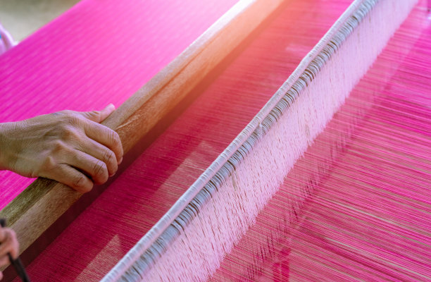 在织布机上工作的妇女，编织手工织物。纺织织造。用传统手工织布机在长棉线上织造。泰国的纺织品生产。亚洲文化。图片下载