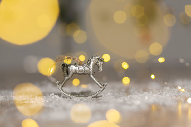 圣诞主题的装饰小雕像。摇摆木马的小雕像。装饰圣诞树。节日装饰，温馨的散景灯。图片下载