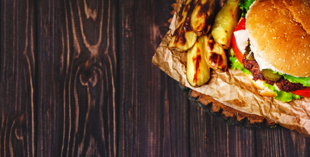 家庭制作的牛肉汉堡与生菜和蛋黄酱在小木砧板上的特写。暗的背景图片下载