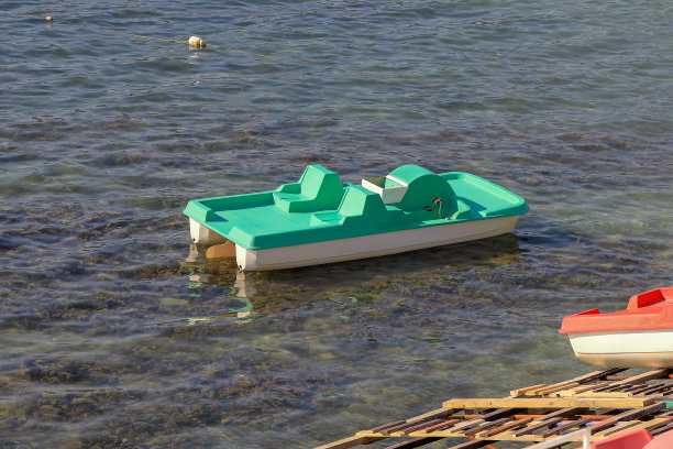 一艘绿色的塑料双体船在海岸附近的海面上波浪起伏图片下载