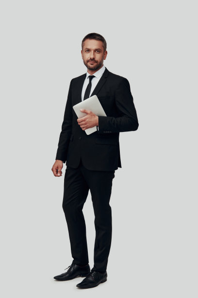 全长迷人的年轻男子在全看着相机，拿着数字平板电脑，而站在灰色的背景图片下载