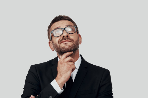 迷人的年轻男子在全西装保持手下巴和看别处，而站在灰色的背景图片下载