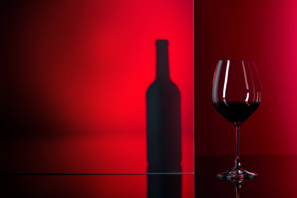 红色背景上的一瓶和一杯红酒。图片下载