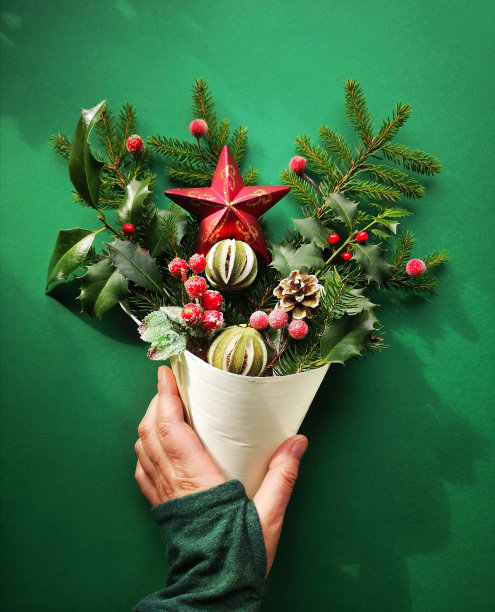 圣诞装饰品，冷杉树枝，浆果，冬青，干酸橙和星在手里，平躺在绿色的纸背景图片下载