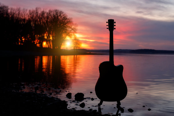 日落时的吉他剪影。海洋和树木的背景。图片下载
